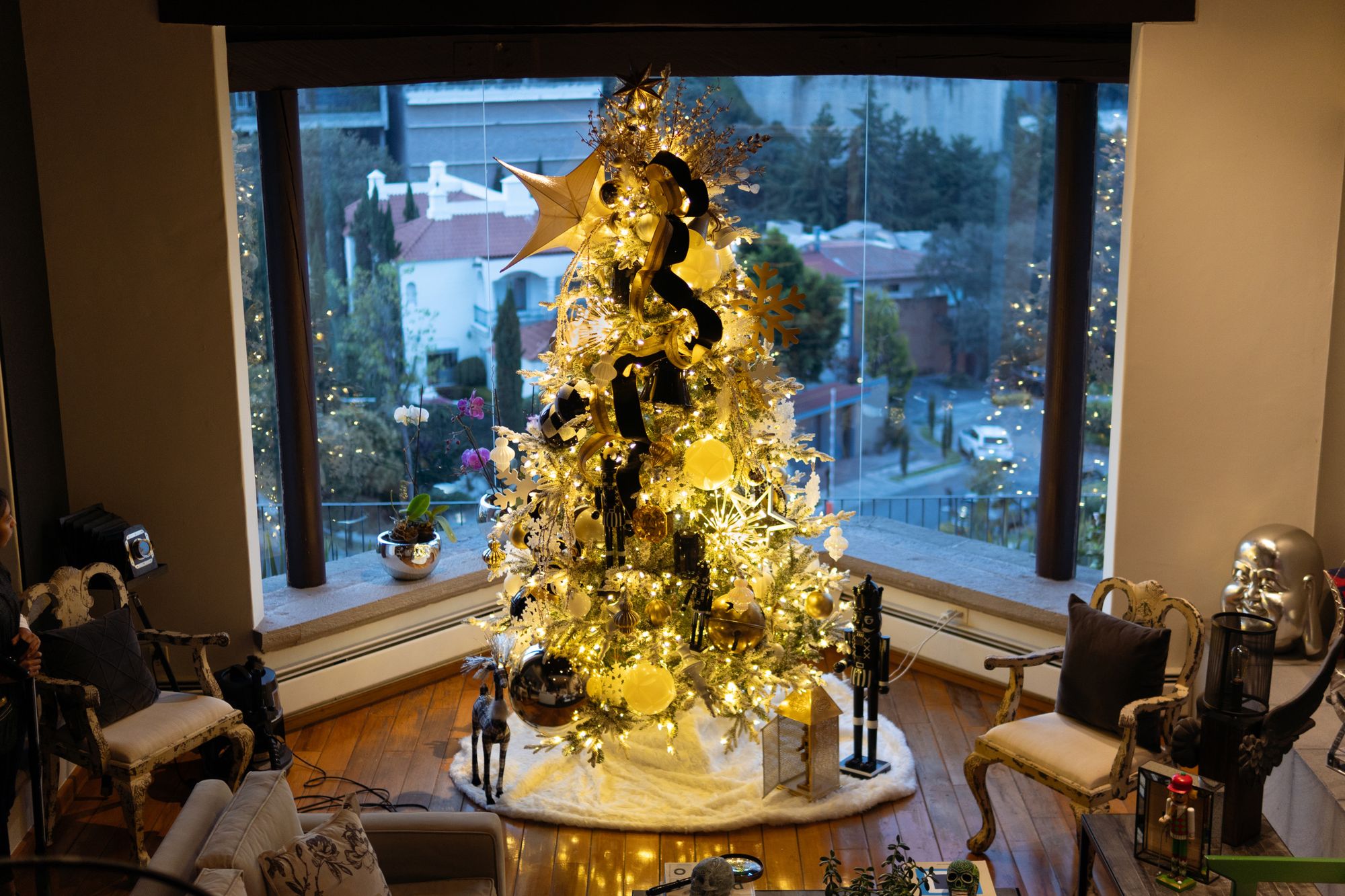 Árbol vestido en dorado, negro y blanco frente a un ventanal, diseñado e instalado por Lucy Perea Decor
